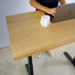 junger mann hinter einem höhenverstellbarem schreibtisch aus massivholz eiche mit baumkante darauf laptop und kaffeetasse