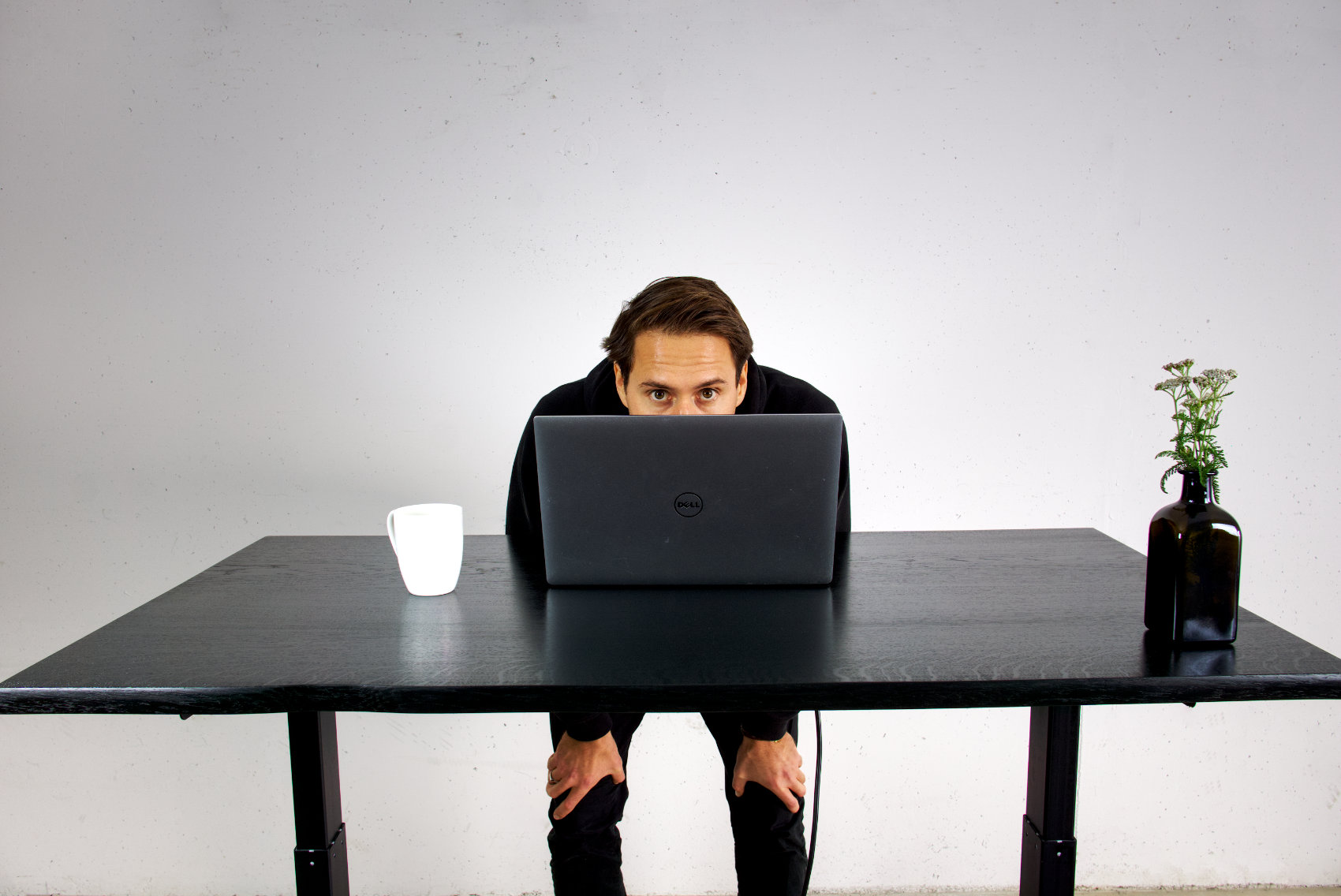 stehtisch in schwarzer eiche massivholz mit baumkante darauf laptop, weiße tasse und ein junger mann dahinter
