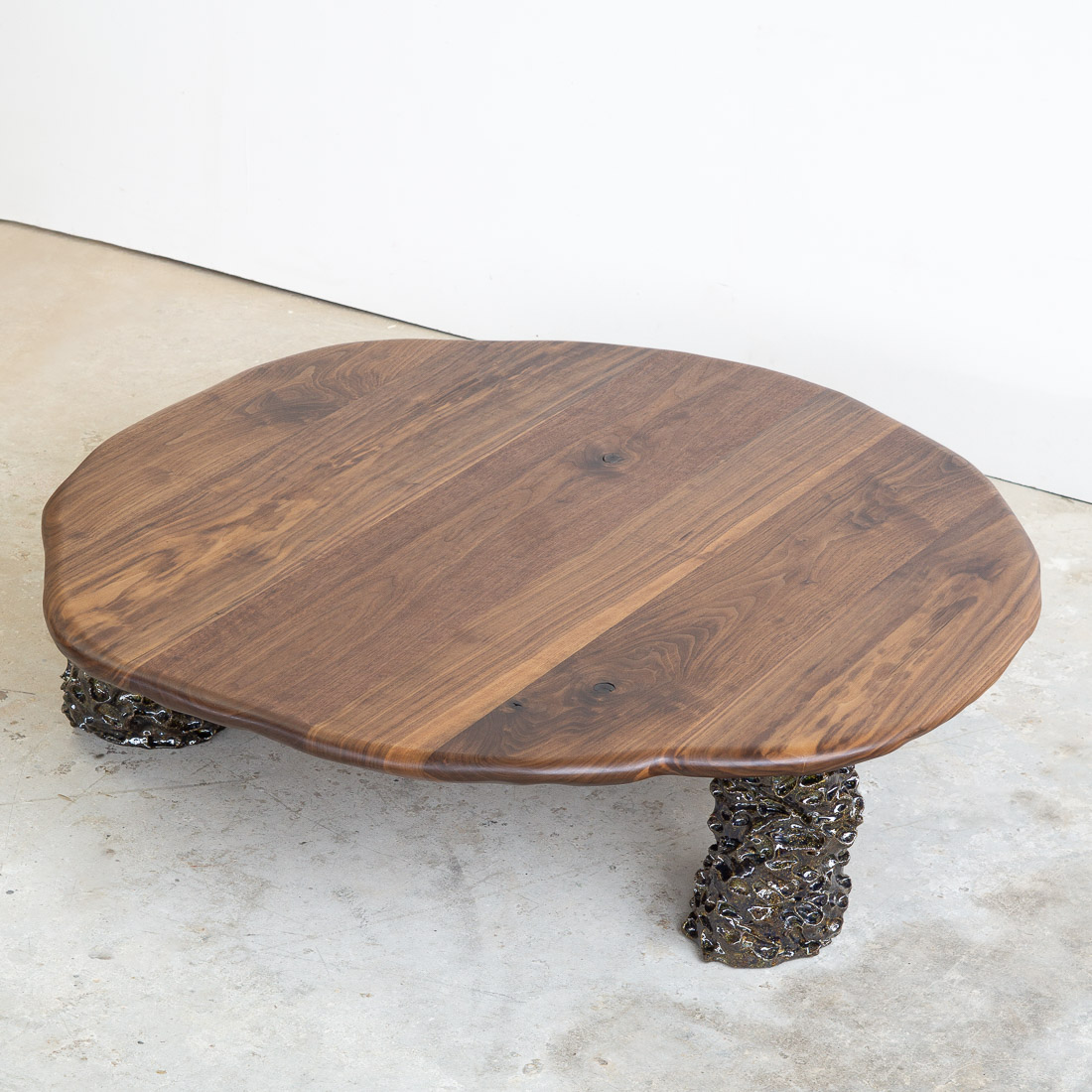 coffee table in walnut with three sculptural legs made of dark green ceramic
